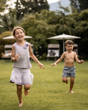 Familienurlaub im Hotelgarten in Naturns Zwei Kinder laufen barfuß über den Rasen im Hotelgarten zwischen Liegen und Sonnenschirmen.
