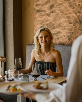 Genuss im Hotelrestaurant im Feldhof Ein Paar sitzt im Hotelrestaurant beim Abendessen, während ein Kellner den Tisch bedient.