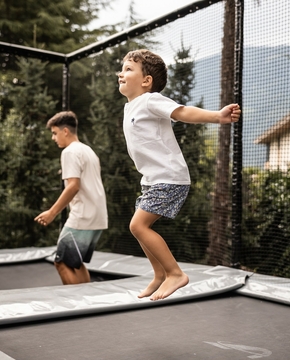 Familienurlaub in Südtirol auf dem Trampolin Drei Kinder springen gemeinsam auf einem Trampolin im Garten vor dem Hotel.